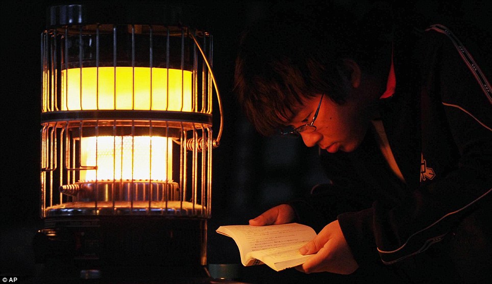 Contrast: An evacuee from a junior high school studies under the light of a kerosene stove at a makeshift shelter in stricken Ofunato