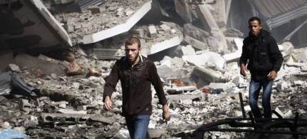 Palestinians walk through the debris after an Israeli air strike on a building in Gaza City Sunday. (photo: Adel Hana/AP)